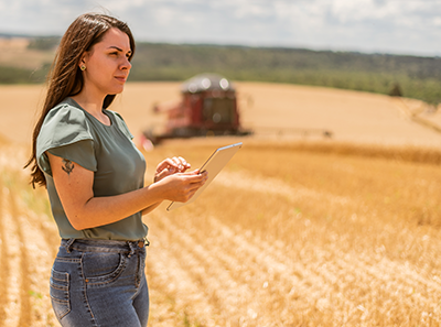 IMAGE: woman in wheatfield reading with combine in background.