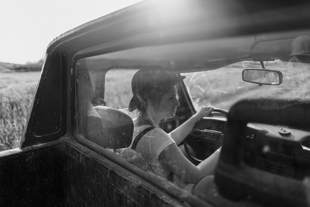 IMAGE: smiling woman driving as viewed through the back window of a pickup